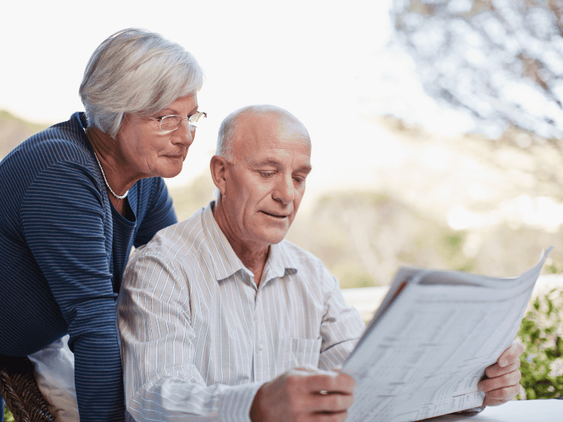 retirement planning classes - retired couple at table, husband is reading the paper and his wife is reading it over his shoulder.