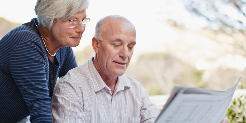 retirement planning classes - retired couple at table, husband is reading the paper and his wife is reading it over his shoulder.