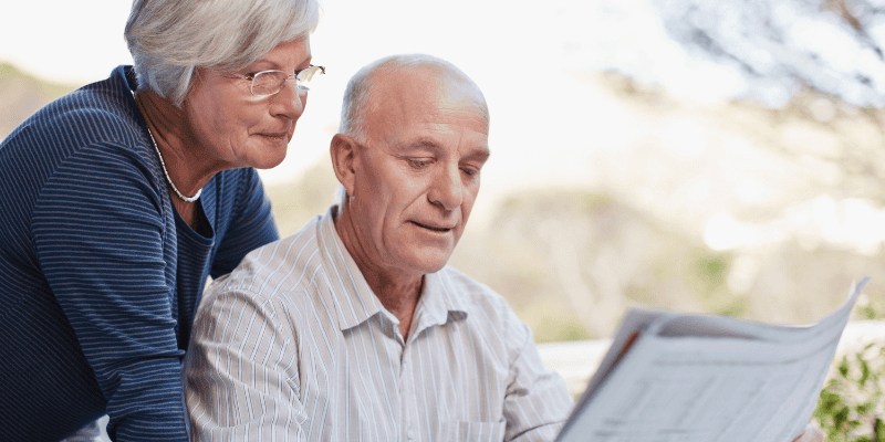 retirement planning classes - retired couple at table, husband is reading the paper and his wife is reading it over his shoulder.